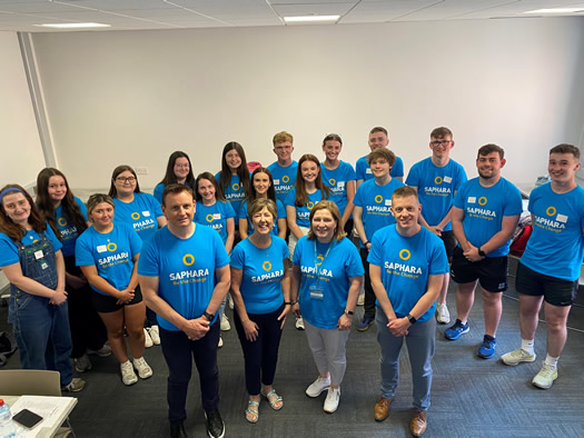 Saphara's newcomer welcome week with students from St Mary's and Stranmillis Colleges and staff from Saphara all standing together in a room with Saphara - Be the change t-shirts on