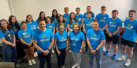 Saphara's newcomer welcome week with students from St Mary's and Stranmillis Colleges and staff from Saphara all standing together in a room with Saphara - Be the change t-shirts on