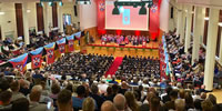 Graduation ceremony at Whitla Hall, Queen's University.  Taken from the balcony with family and friends of the students looking on and the graduates of the day on the lower floor space, seated with their graduation gowns on.  On the stage in front of them are the faculty of Queens and some of St Mary's taking part in the graduation ceremony.