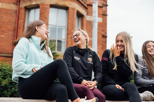 Picture of four students sitting outside of St Mary's university college laughing