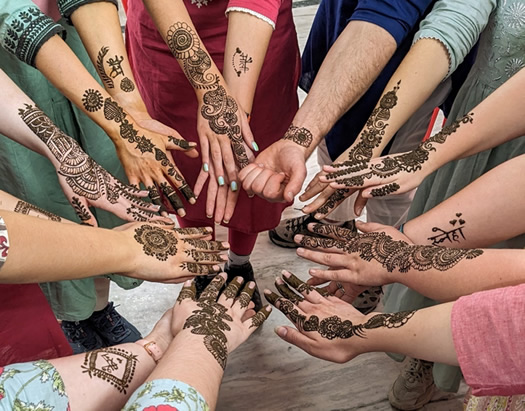 A circle of hands all coming together in the middle.  Each hand is intricately tattooed with a henna design.