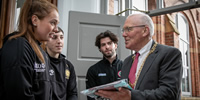 Picture of High Sheriff of Belfast, Dr John Kyle at the doors of St Mary's with three of the Student Union Excutive and being presented with a College sports jersey